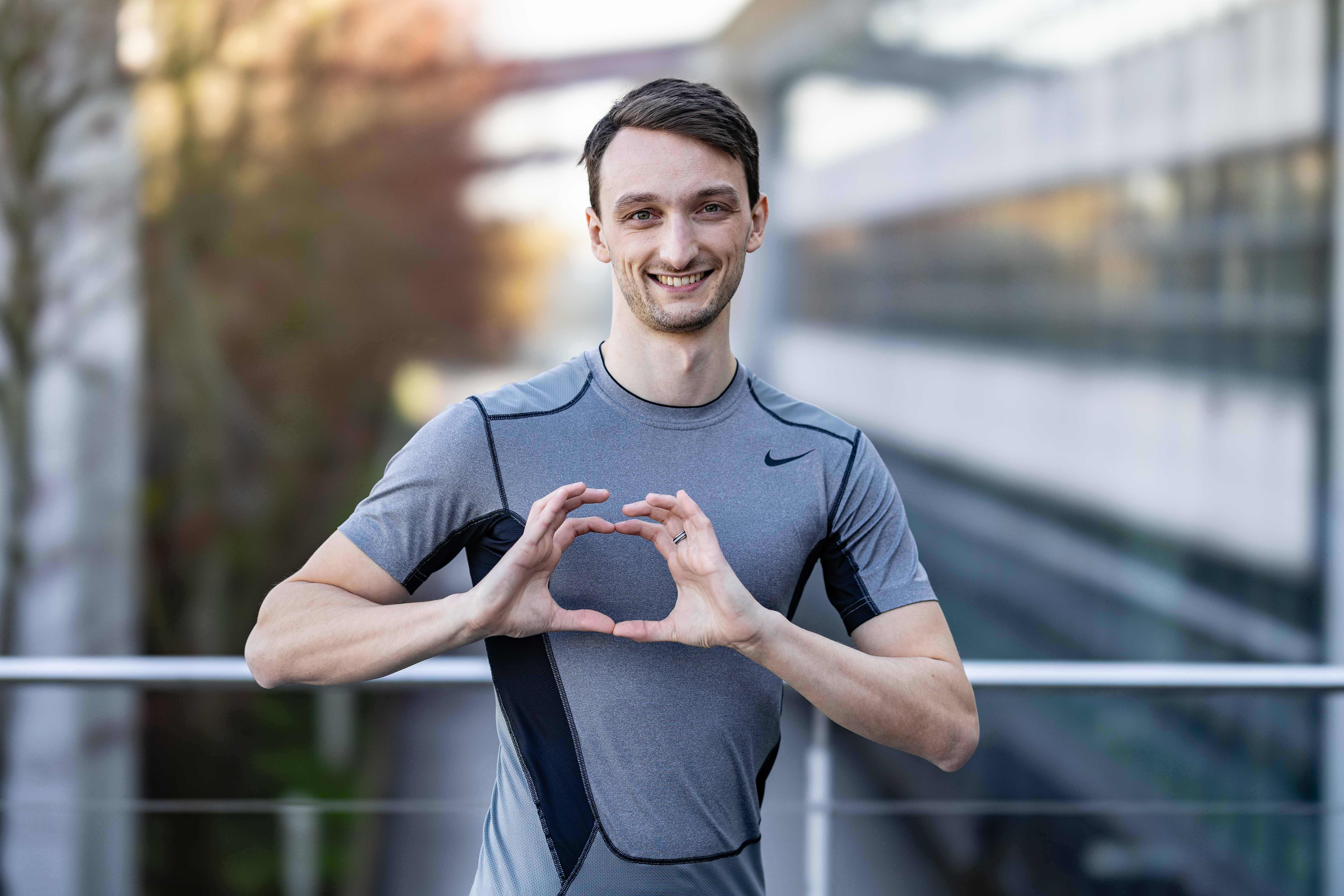 Homme souriant formant le logo OneHealth avec les mains, portant une tenue de sport.
